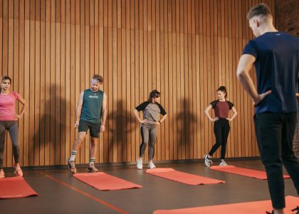 A group exercise class with a personal trainer leading stretching exercises in a gym.