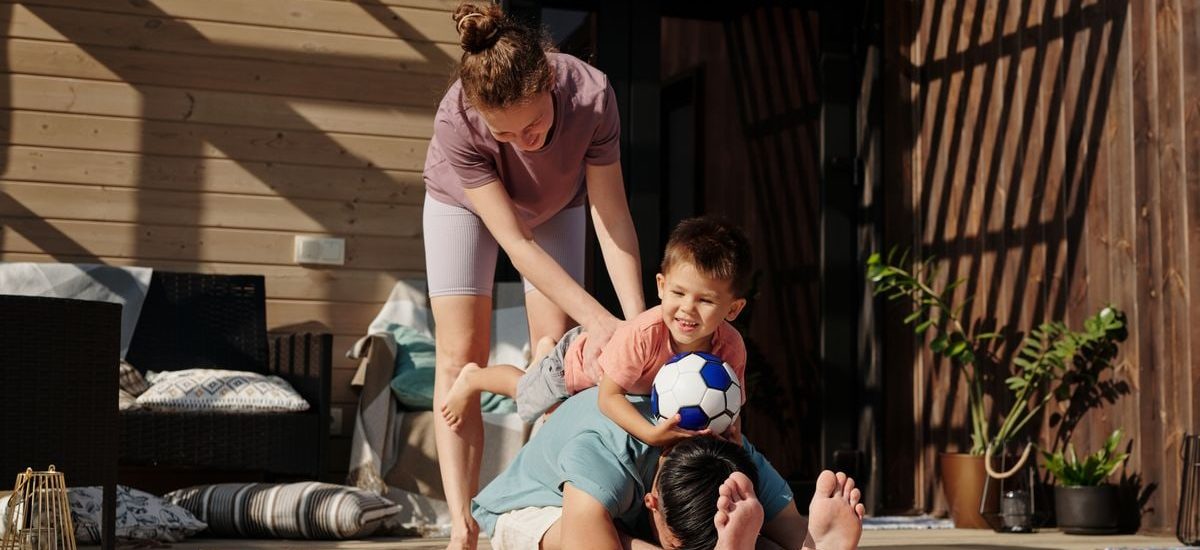 Family engaging in playful yoga on a sunlit porch, bonding and exercising together.