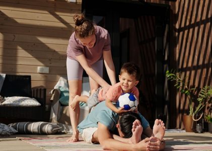 Family engaging in playful yoga on a sunlit porch, bonding and exercising together.